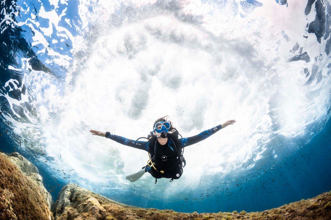 A diver drifting under a breaking wave, arms outstretched